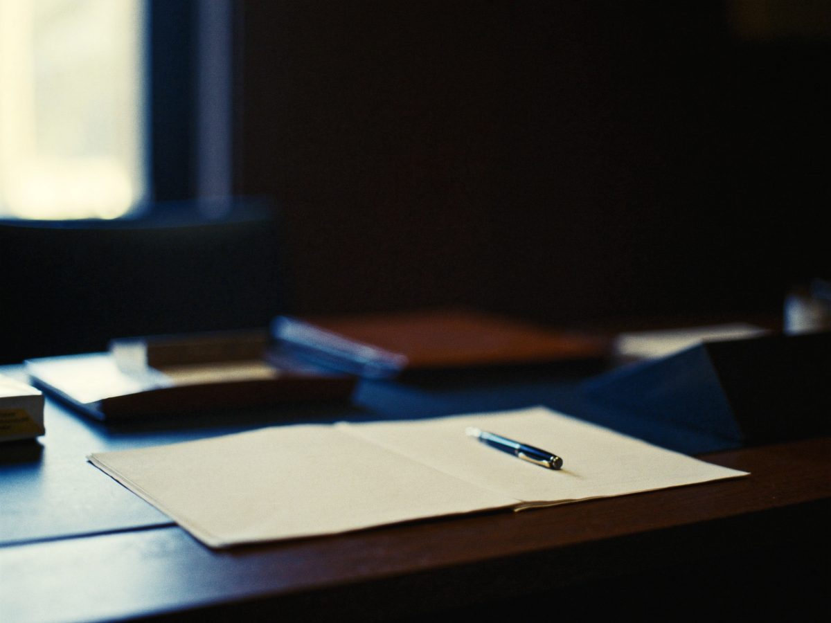 A folder of records, papers, and a pen resting on a desk in soft light